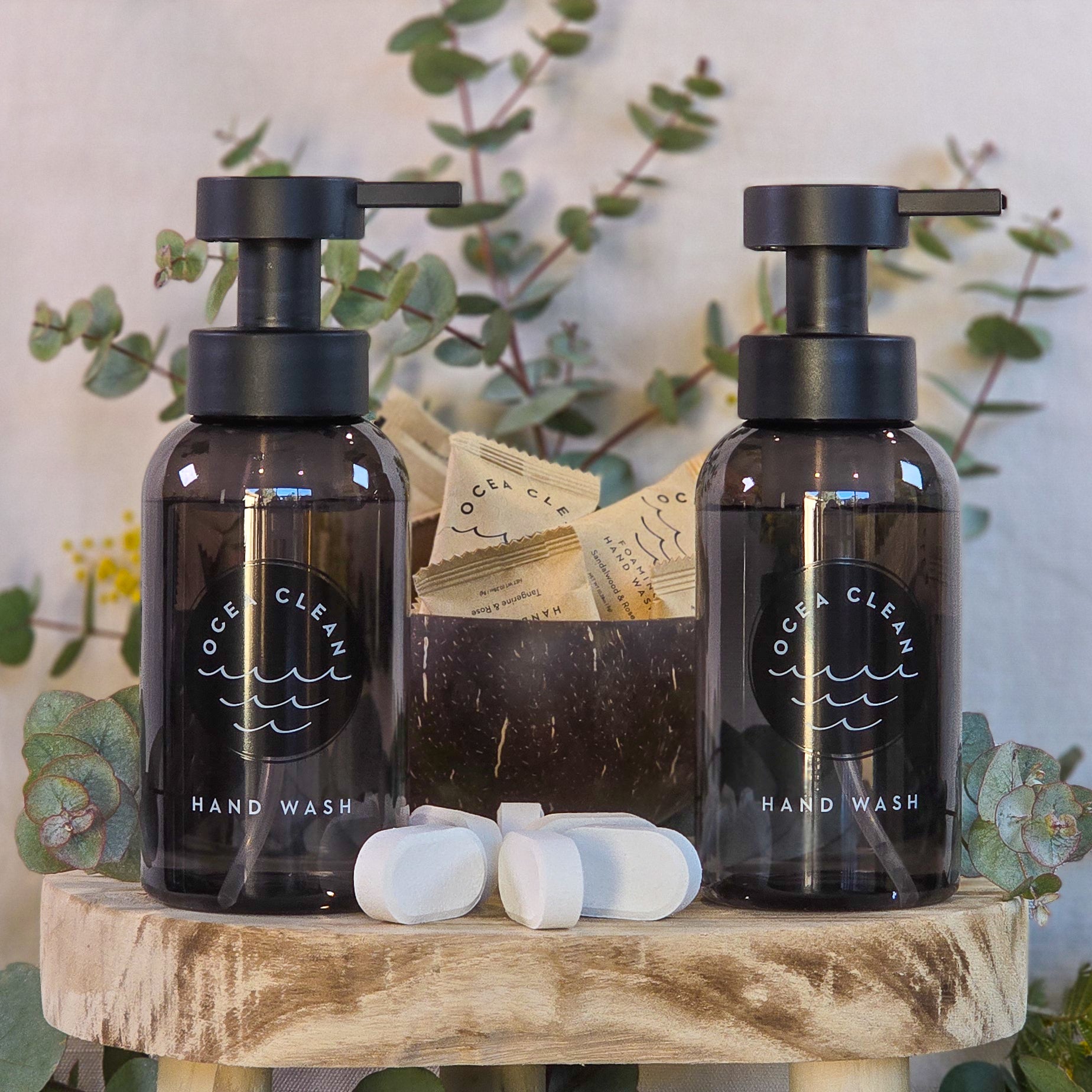 Two bottles of Ocea Clean hand wash on a wooden stand with eucalyptus leaves in the background.