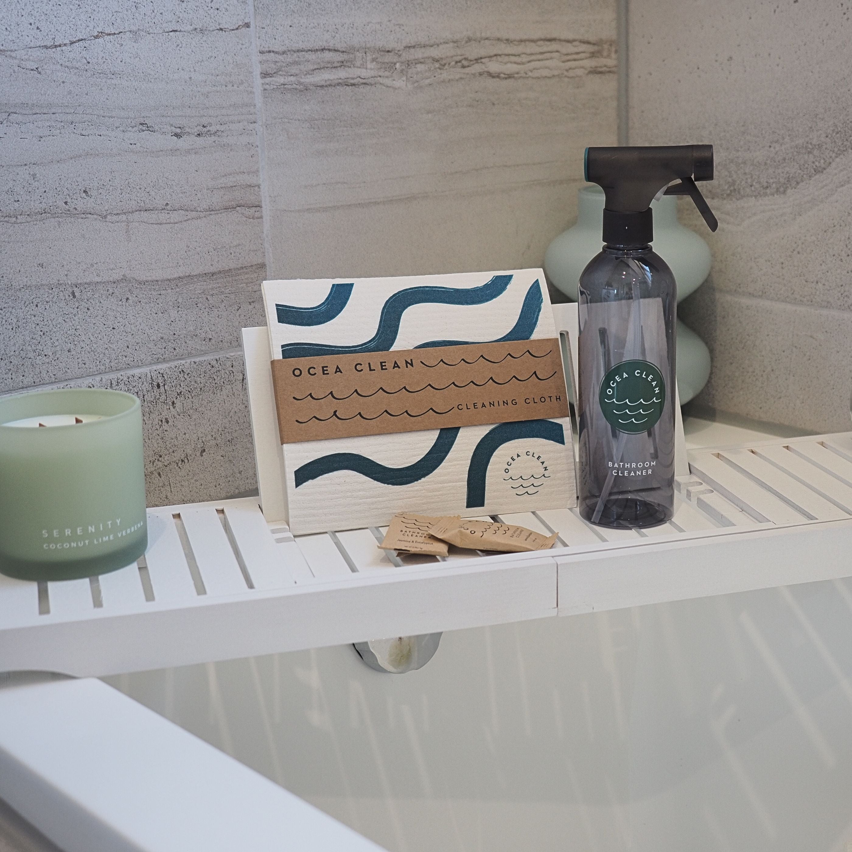 Ocea Clean cleaning supplies featuring a spray bottle, cleaning cloths, and a candle on a bathtub ledge.