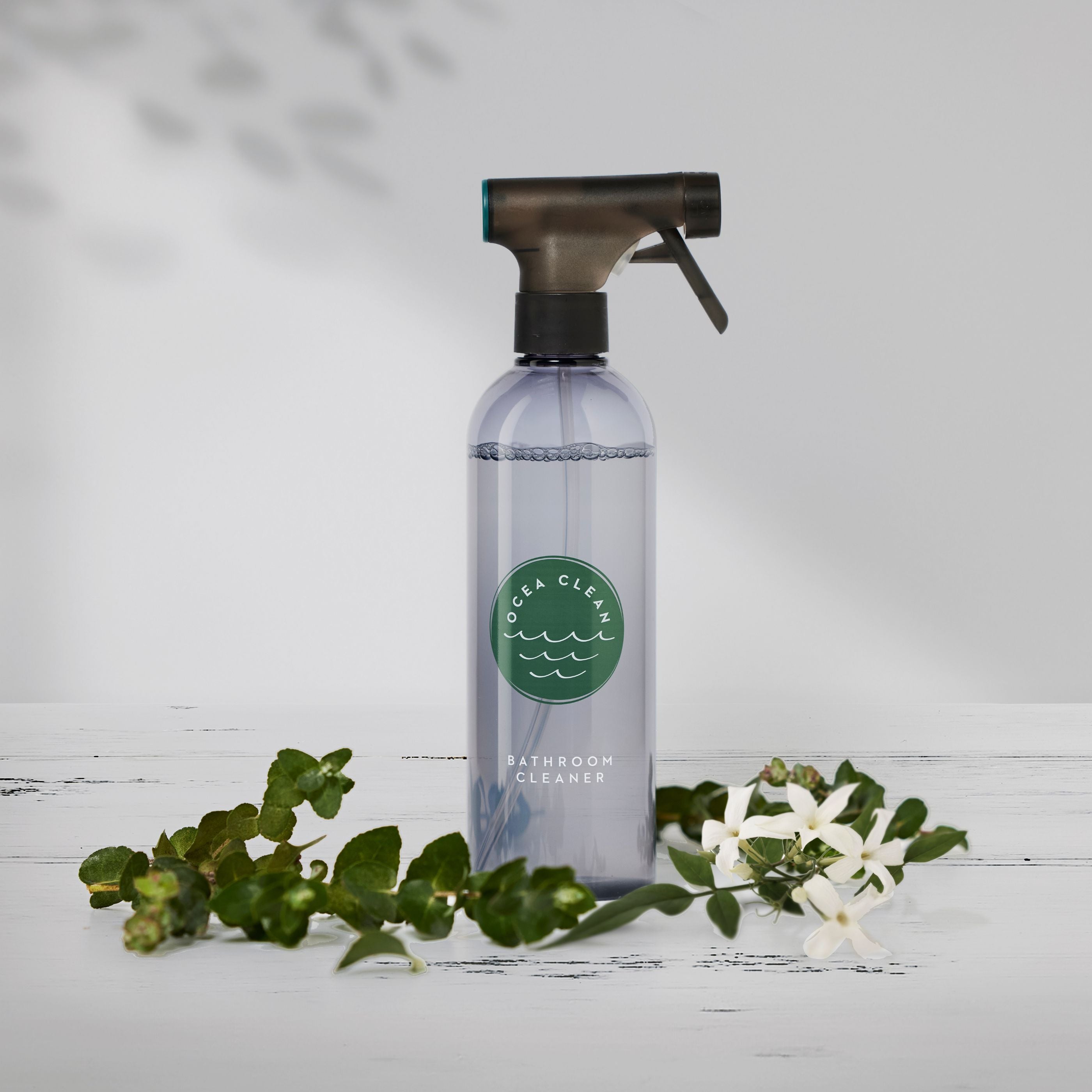 Ocea Clean Bathroom Cleaner in a spray bottle, surrounded by greenery and white flowers, showcasing eco-friendly cleaning.
