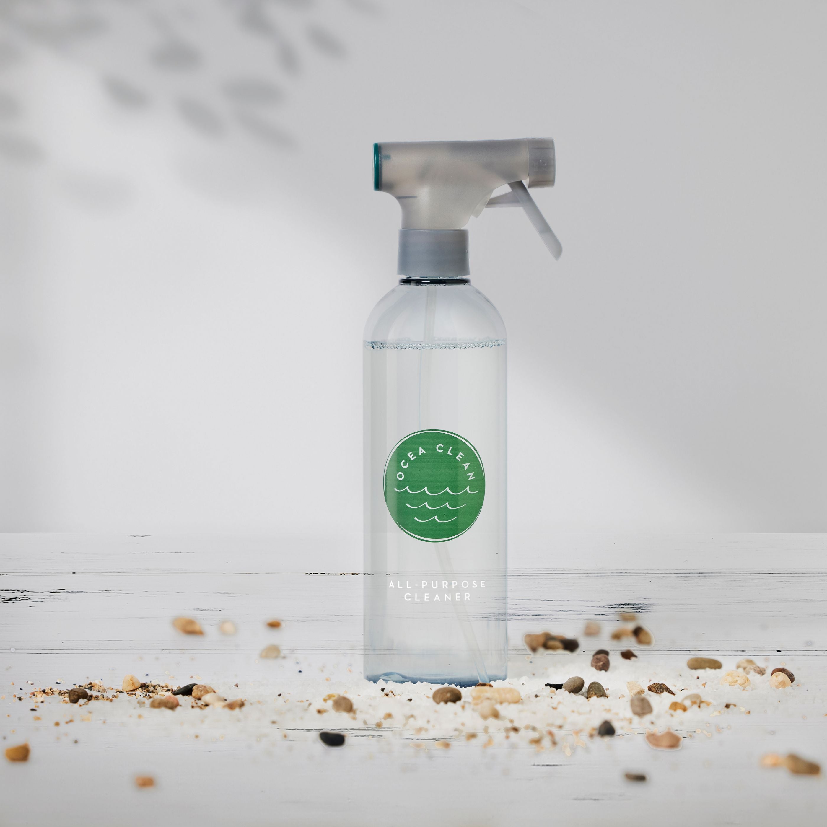 Clear spray bottle of Ocea Clean All-Purpose Cleaner against a neutral background with scattered pebbles.