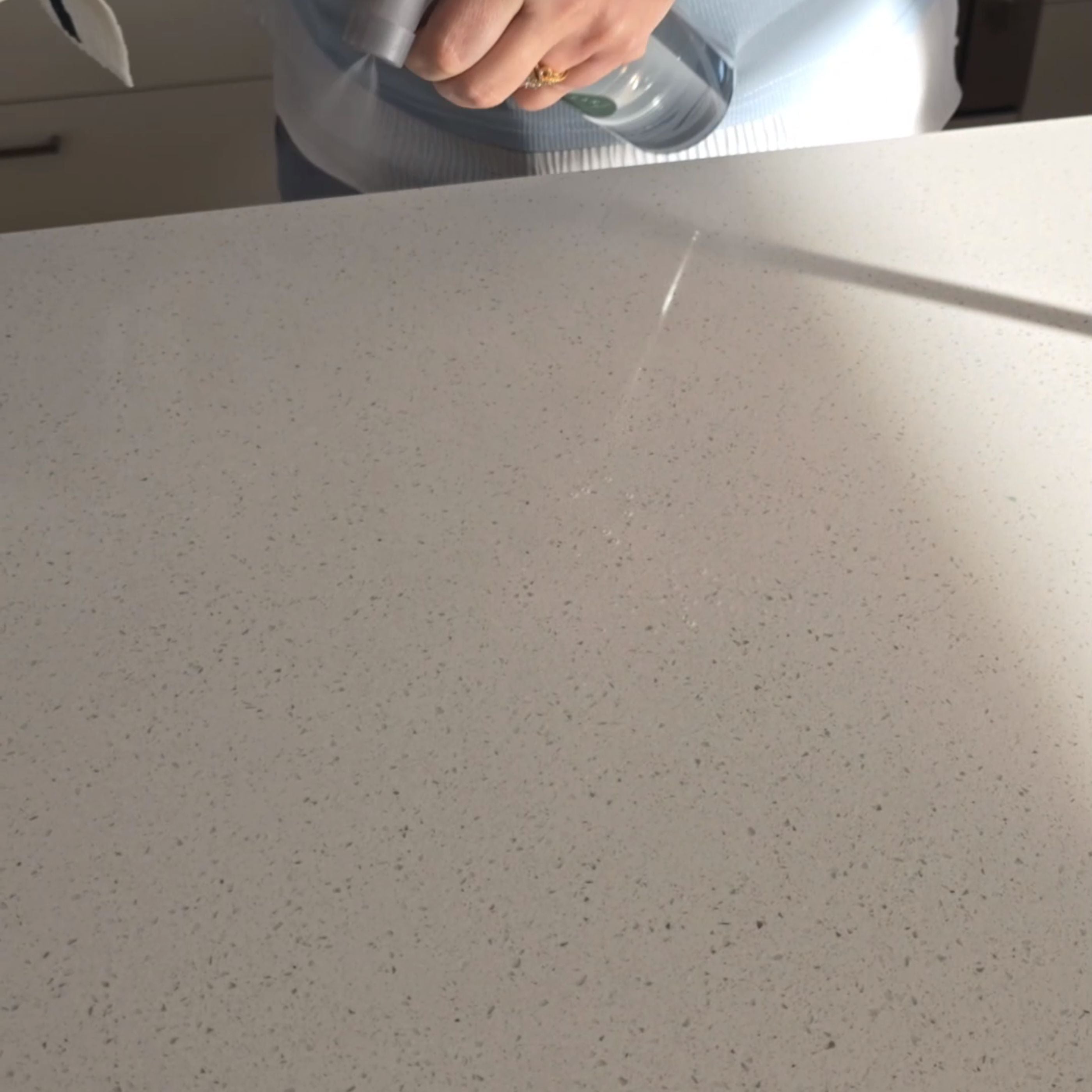 Person using an all-purpose cleaner spray on a clean, white countertop.